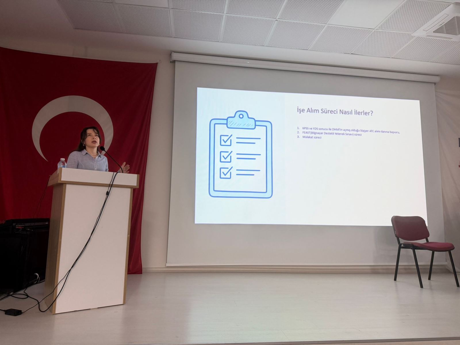 İşe alım sürecindeki KPSS, FEAST ve mülakat aşamalarının anlatıldığı bu karede, bir kadın konuşmacı süreci detaylandırırken görülüyor. Ekranda yer alan kontrol listesi görseli, sunumun yapılandırılmış ve adım adım ilerleyen eğitici yönünü vurguluyor.